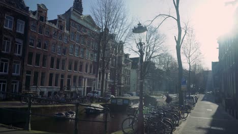 Leerer-Amsterdamer-Kanal-An-Einem-Kühlen-Wintertag-Mit-Häusern-Und-Sonne,-Die-Einen-Blendenfleck-Erzeugen