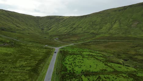 Drone-shot-of-a-car-driving-towards-Glenniff-Horseshoe,-stationary-while-the-car-drives-along-the-road