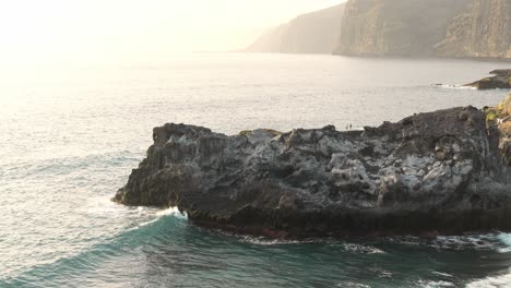 Meereswellen-In-Zeitlupe-Waschen-Felsige-Klippen,-Helles-Sonnenlicht-Im-Hintergrund