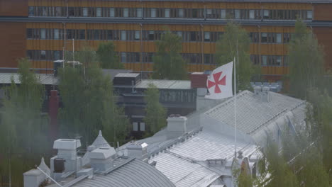 Old-templar-flag-waving-attached-to-pole-on-rooftop-building,-telephoto-close-up