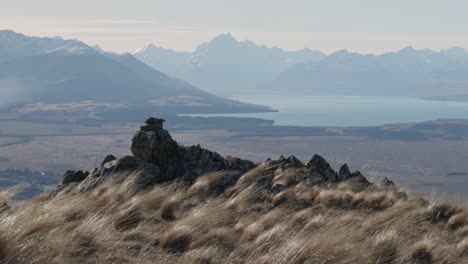 Magnificent-Mount-Cook-and-Lake-Pukaki-visible-in-hazy-distance-on-sunny,-windy-day-in-mountains