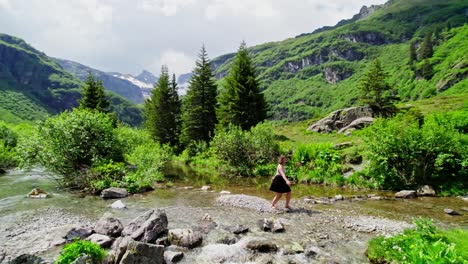Caucasian-woman-dancing-in-alpine-stream,-verdant-summer-scene