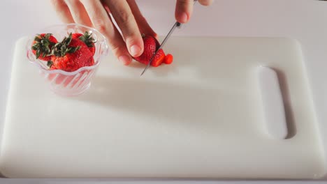 Whole-strawberies-are-placed-on-cutting-board-and-sliced-with-knife,-stem-discarded