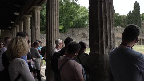 Tourists-Wearing-Earpieces-Listening-To-Guide-Standing-Beside-Stone-Columns-At-Quadriporticus-of-the-Theatres-In-Pompeii