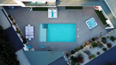 Top-down-shot-of-a-drone-ascending-to-the-terrace-of-a-residential-house-with-a-deflated-swimming-pool-and-sun-loungers-spread-around-it