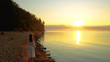 A-girl-in-a-white-dress-stands-by-the-sea-and-gazes-at-the-rising-orange-sun