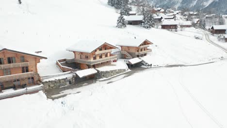 Drone-flying-towards-a-couple-of-chalets-in-a-Swiss-rural-town-in-winter