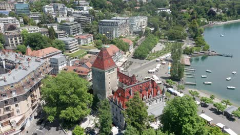 Drone-flying-away-from-tower-of-Chateau-d'Ouchy-and-revealing-the-city-of-Lausanne,-Switzerland