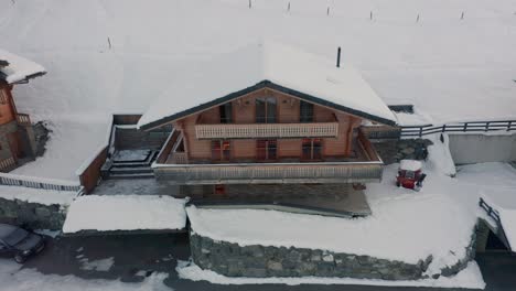 Drone-flying-away-from-snow-covered-rooftop-of-luxurious-chalet