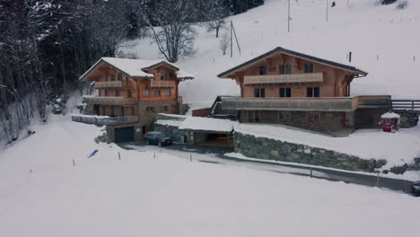 Aerial-of-car-driving-up-to-beautiful-chalet-and-parking-in-garage-in-a-snow-covered-landscape