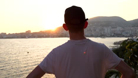 Saranda,-man-watching-the-beautiful-sunset-over-the-buildings-and-the-sea