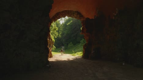 Man-walking-through-a-tunnel-with-his-dog-towards-sunny-and-green-nature
