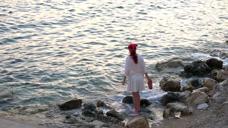 A-girl-in-a-red-scarf-walks-on-the-stone-beach-of-Saranda