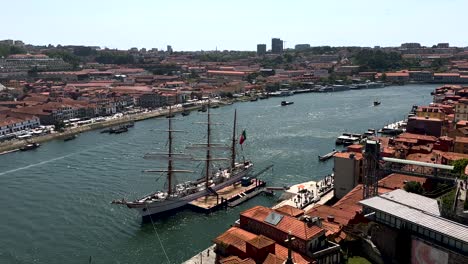 Aerial-panoramic-shot-of-Duoro-River-with-docking-NRP-Sagres-Ship-in-city-of-Porto-during-sunny-day,-Portugal---Roof-tops-and-Vila-Nova-de-Gaia-in-background