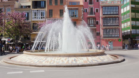 A-charming-fountain-in-Palma-de-Mallorca,-with-passersby-and-colorful-buildings-forming-a-vibrant-backdrop