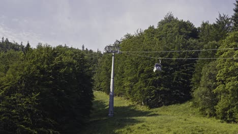 Cable-car-slowly-ascending-through-green-forests-on-a-summer-day