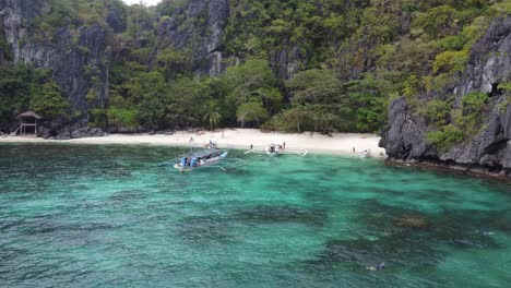 Island-Hopping-Boats-and-people-snorkeling-in-tropical-clear-blue-water-of-Serenity-Beach-on-Cadlao-Island-in-El-Nido,-Philippines