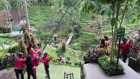 Behind-the-scenes-rearview-of-Girls-in-colorful-long-dress-taking-photo-shoot-riding-a-Giant-swing-over-rice-terraces-in-Alas-Harum,-Ubud-Bali