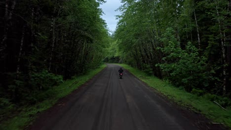 Man-rides-motorcycle-down-lush-green-dirt-road-in-rural-mountains