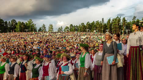 Lapso-De-Tiempo-De-La-Multitud-En-Movimiento-Masiva-Reunida-En-El-Festival-De-Danza-Y-Canto-Letón-Con-Nubes-En-Movimiento-Durante-La-Puesta-De-Sol-En-Riga,-Letonia