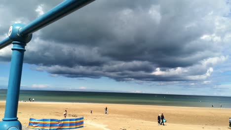 Looking-through-metal-railings-at-ominous-storm-cloud-approaching-golden-sandy-Anglesey-beach