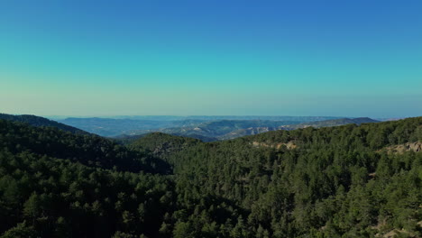 Drone-view-tilting-up-of-mountains,-valleys-and-several-more-mountains-in-the-distance-amid-a-clear-blue-sky