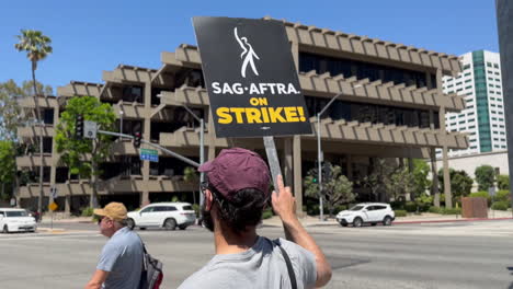 A-SAG-AFTRA-striker-pumping-fist-and-holding-picket-sign-outside-Warner-Brothers-Gate-4---Gimbal-Shot-at-Olive-Ave-and-Hollywood-Way-Intersection-in-Burbank,-CA-at-around-11:30-AM-on-7-19-2023