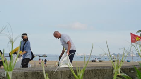 Menschen-Räumen-Müll-Am-Strand-Auf,-Im-Hintergrund-Eine-Vietnamesische-Flagge
