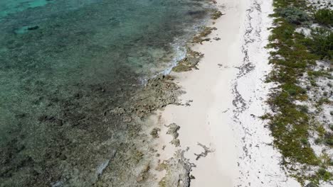 Drohnenaufnahmen-Neigen-Sich-Langsam-Nach-Oben-Und-Zeigen-Wellen,-Die-über-Einem-Korallenriff-In-Einem-Wunderschönen-Tropischen-Ozean-Brechen,-Mit-Fußabdrücken-Im-Sand-Am-Strand-Der-Kaimaninseln-In-Der-Karibik