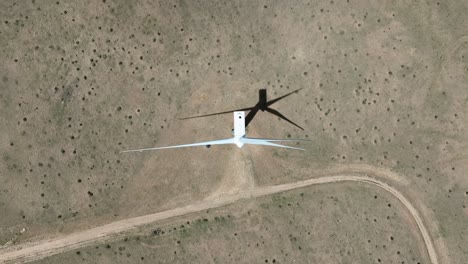 Top-down-shot-of-wind-turbine-spinning-and-casting-shadow-and-sandy-desert-ground