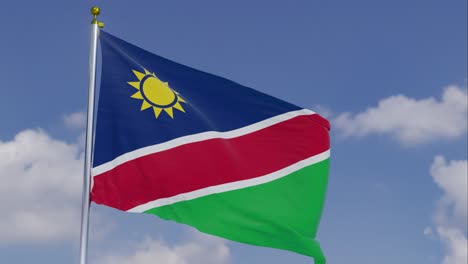 Flagge-Namibias-Bewegt-Sich-Im-Wind-Mit-Einem-Klaren-Blauen-Himmel-Im-Hintergrund,-Wolken-Bewegen-Sich-Langsam,-Fahnenmast,-Zeitlupe