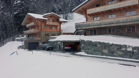 Drone-following-driving-car-that-parks-in-garage-of-luxurious-chalet-in-snow-covered-landscape