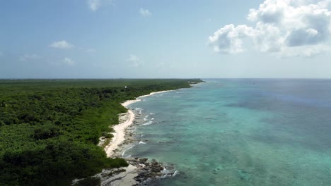 Drohnenaufnahmen,-Die-Nach-Links-über-Einen-Türkisfarbenen-Ozean-Und-Ein-Korallenriff-In-Der-Karibik-Rollen,-Mit-Einheimischen-Wäldern,-Die-Sich-Entlang-Des-Strandes-Bis-Zum-Horizont-Erstrecken,-Während-Wolken-Schatten-über-Das-Wasser-Werfen