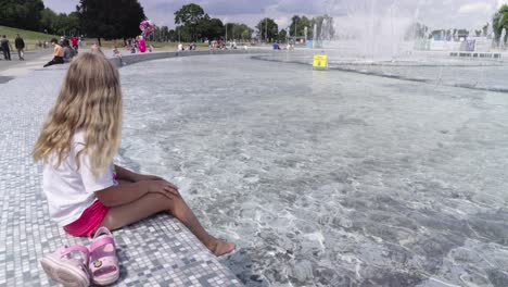 A-little-girl-dips-her-bare-feet-in-the-city-fountain-in-the-centre-of-Warsava