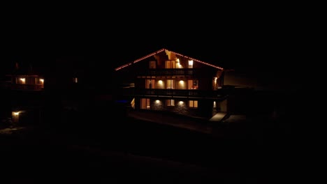 Aerial-dolly-of-beautiful-chalet-with-burning-lamps-and-Christmas-lights-at-night