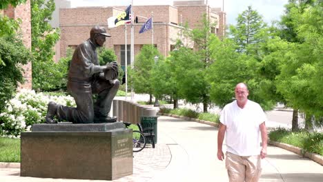 Statue-of-Notre-Dame-University-football-coach-Frank-Leahy-on-the-campus-of-Notre-Dame-University-in-South-Bend,-Indiana-with-man-walking