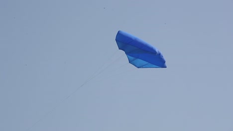 Many-participants-are-flying-their-kites-in-the-International-Kites-Festival,-one-of-which-is-flying-a-blue-parachute-like-kite-high-in-the-sky