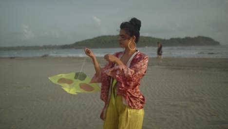 A-young-Asian-adult,-donning-a-contemporary-attire-and-showcasing-a-distinctive-hairstyle,-stands-on-a-breezy-beach,-grappling-with-the-challenge-of-flying-her-kite