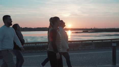 Young-people-are-walking-along-a-road-with-a-river-and-a-sunset-in-the-background