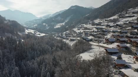 Drone-flying-over-snow-covered-forest-near-an-idyllic-Swiss-mountain-town-in-winter