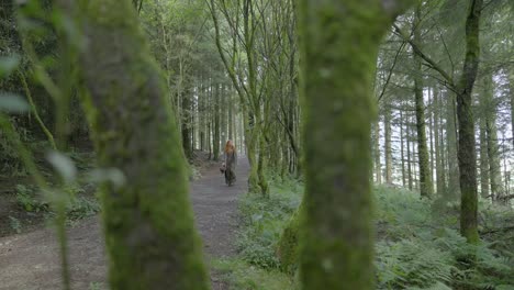Girl-walking-along-shady-forest-path-with-view-between-mossy-branches-at-half-speed-slow-motion