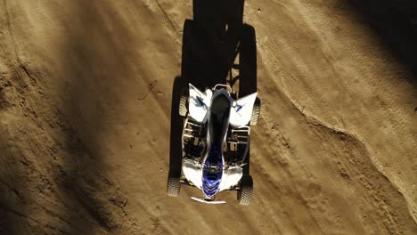Abstract-goldehour-drone-spinning-push-in-shot-of-blue-and-white-atv-all-terrain-vehicle-quad-standing-on-dirt