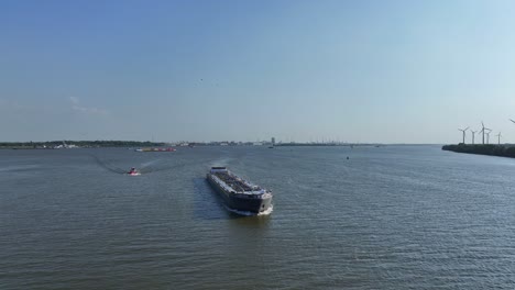 Tanker-ship-sailing-through-the-river,-wind-farm-at-background,-Aerial-view