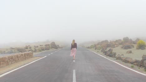 Chica-Con-Falda-Rosa-De-Verano-Caminando-Por-La-Carretera,-Desapareciendo-En-Una-Niebla-Misteriosa