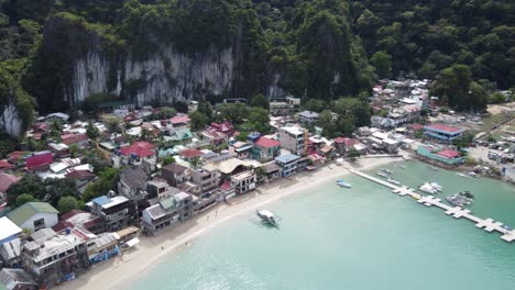 Aerial-view-:-Pier-and-beachfront-port-of-El-Nido-Town-proper-ahead-of-lush-tropical-background-of-towering-limestone-rocks,-Bacuit-Bay---Philippines