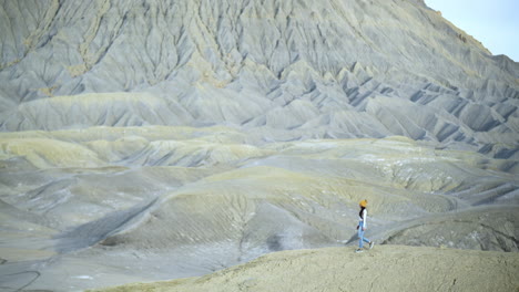 Junge-Frau,-Die-Allein-Auf-Einem-Sandsteinhügel-In-Der-Grauen-Wüstenlandschaft-Von-Utah,-USA,-Spaziert