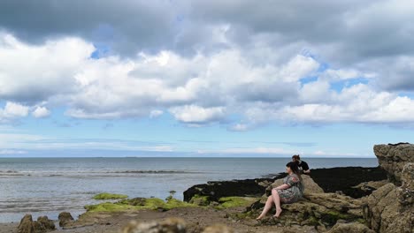 Young-couple-taking-pose-for-model-photographs-on-the-rocks-of-cloudy-Welsh-beach-in-Anglesey