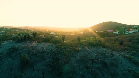 4k-cinematic-drone-reveal-of-colorful-houses-and-neighborhoods-on-the-Caribbean-island-of-Curacao,-during-golden-hour-sunset-with-flare,-orbit-around-hill-with-trees,-foliage-and-cacti