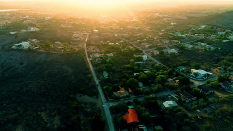 4k-cinematic-drone-tilt-up-of-roads-leading-through-houses-and-neighborhoods-on-the-Caribbean-island-of-Curacao,-during-golden-hour-sunset-with-flare