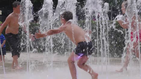 Slow-motion-shot-of-a-boy-in-a-swimsuit-running-through-streams-of-water-in-a-city-fountain